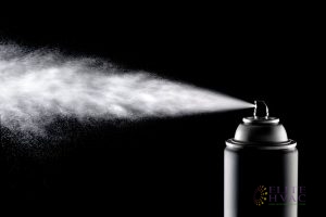 An Aerosol Can Spraying Contents in Front of a Blacklit Background